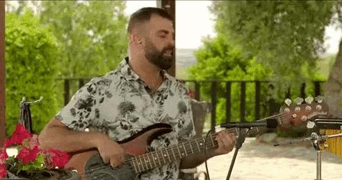 a man with a beard is playing a guitar and singing into a microphone outside .