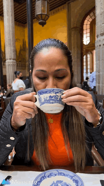 a woman drinking from a blue and white cup with the word momento on the bottom