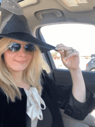 a woman wearing a witch hat and sunglasses is sitting in the back seat of a car
