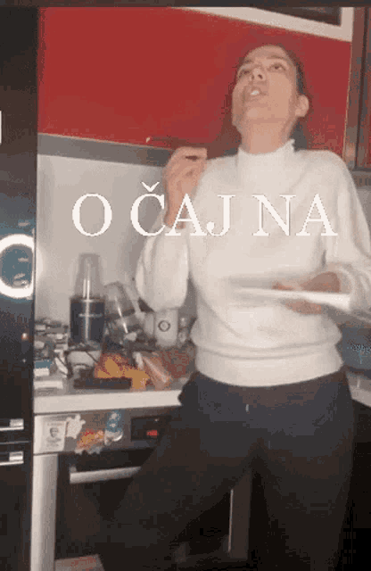 a woman in a white sweater is standing in a kitchen holding a plate with the word očajna on it