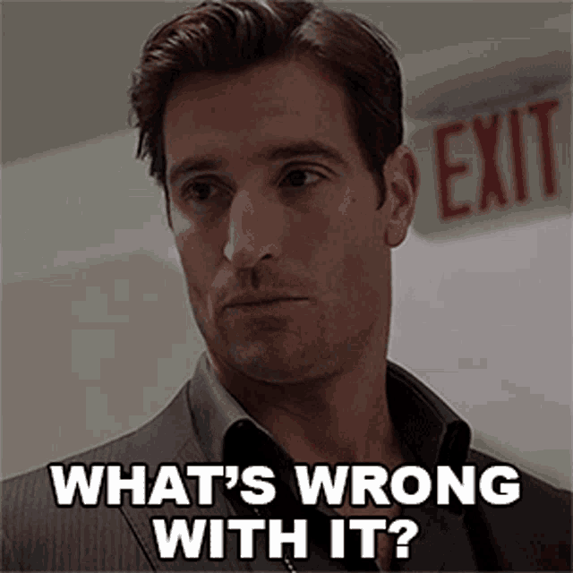 a man in a suit is standing in front of an exit sign and says what 's wrong with it ?