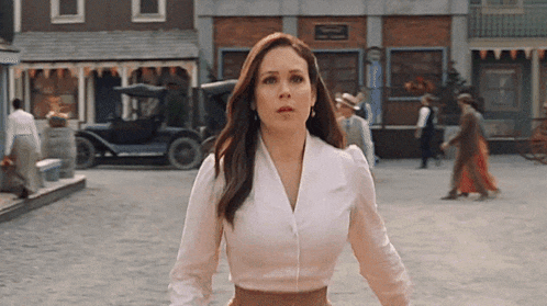 a woman in a white shirt and brown skirt is standing in a street .
