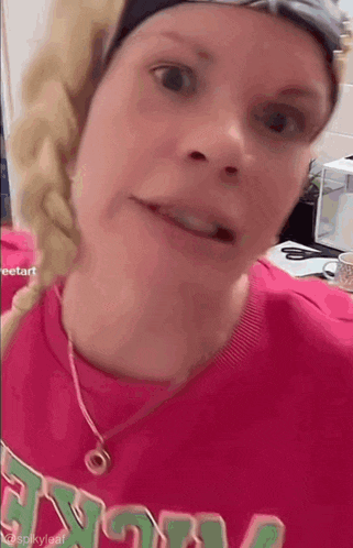 a woman wearing a pink shirt and a necklace is looking at the camera .