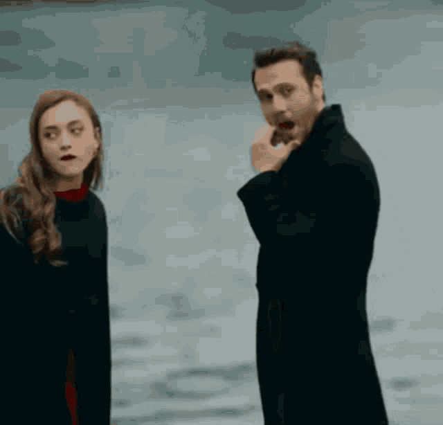 a man and a woman are standing next to each other near the water