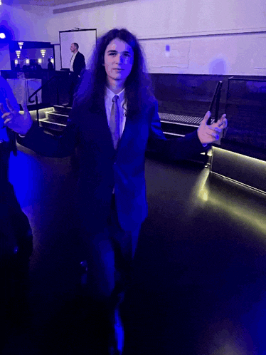 a man with long hair in a suit and tie stands in front of stairs