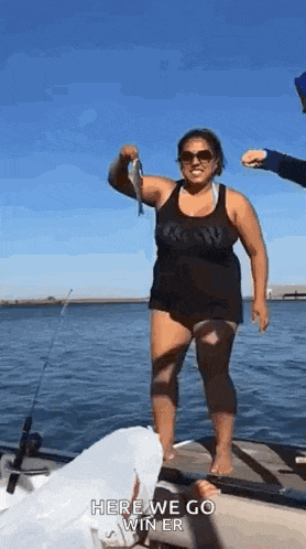 a woman is standing on a dock holding a fish in her hand .
