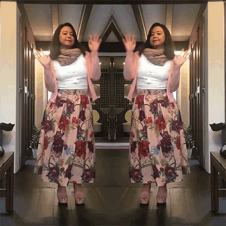 a woman wearing a pink cardigan and a floral skirt stands in front of a mirror