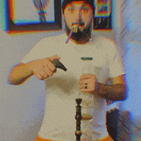 a man with a beard wearing a white shirt and a black hat smoking a cigarette