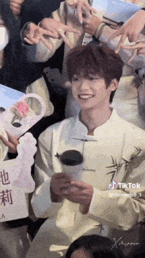 a man in a white shirt is holding a cup of coffee and smiling while standing in front of a crowd of people .