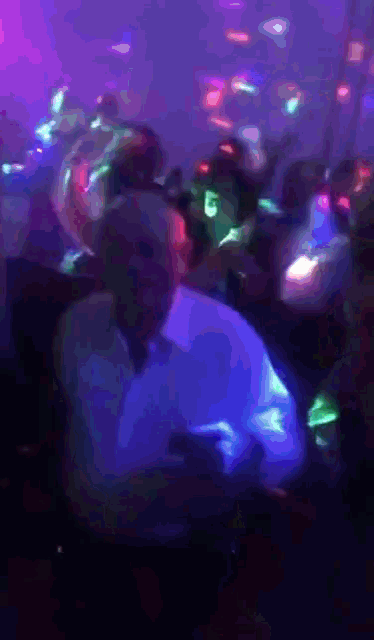 a man in a white shirt is dancing in a dark room with purple and blue lights