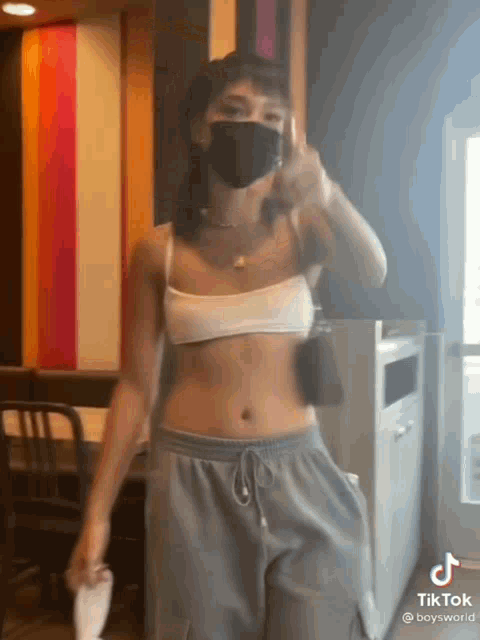 a woman in a crop top and sweatpants is wearing a mask .