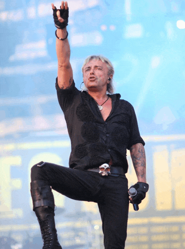 a man in a black shirt with a skull belt buckle stands on one leg
