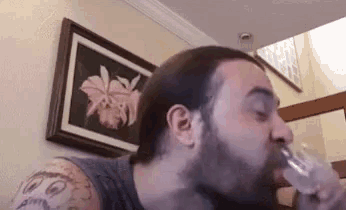 a man with a beard is drinking water from a glass in front of a painting .