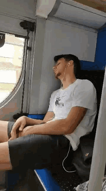 a man is sleeping on a train while listening to music with headphones .