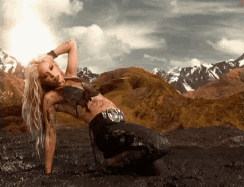 a woman is kneeling down in a muddy field with mountains in the background