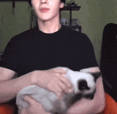 a man in a black shirt is holding a cat in his lap .