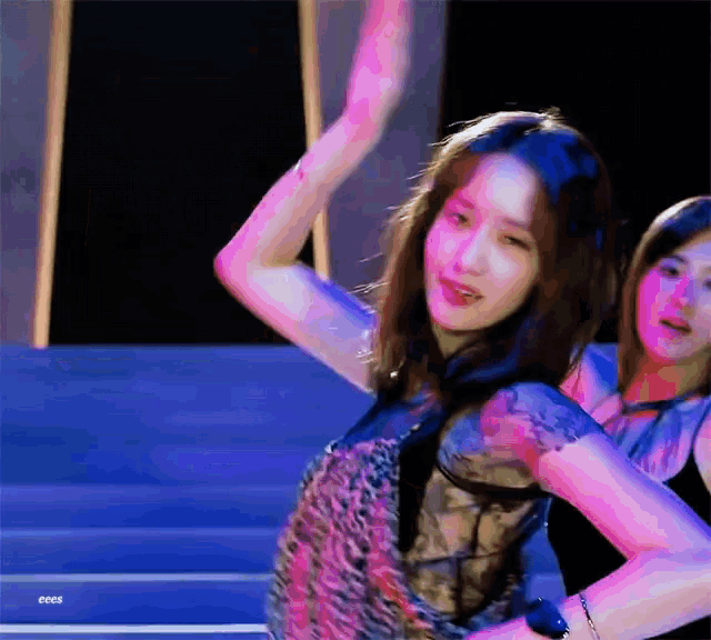 a woman in a leopard print top is dancing with her hands in the air while another woman looks on .