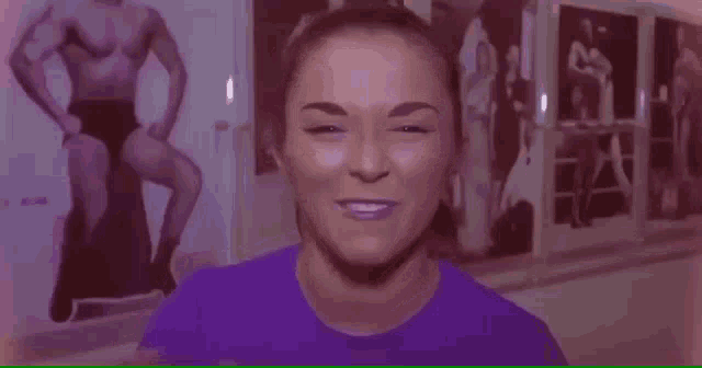a woman in a purple shirt is making a funny face in front of a picture of a man .