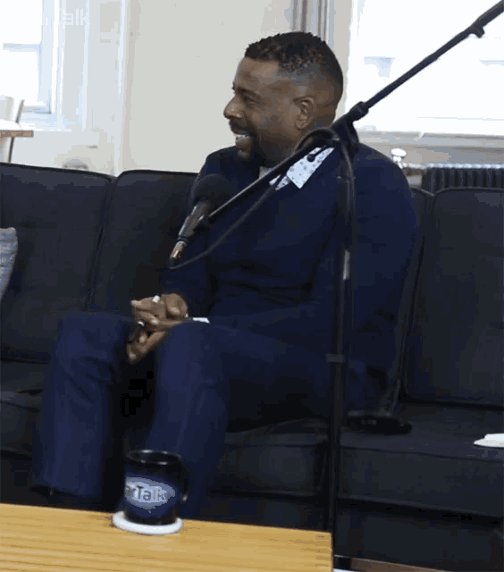 a man sits on a couch with a microphone and a mug that says portalk