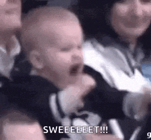 a baby is crying in a crowd of people and a woman is holding it .