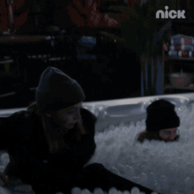 a woman is laying in a hot tub filled with plastic balls and the nick logo is visible in the background