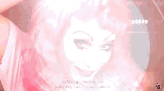 a woman with pink hair is doing drag makeup on her boyfriend 's face ..