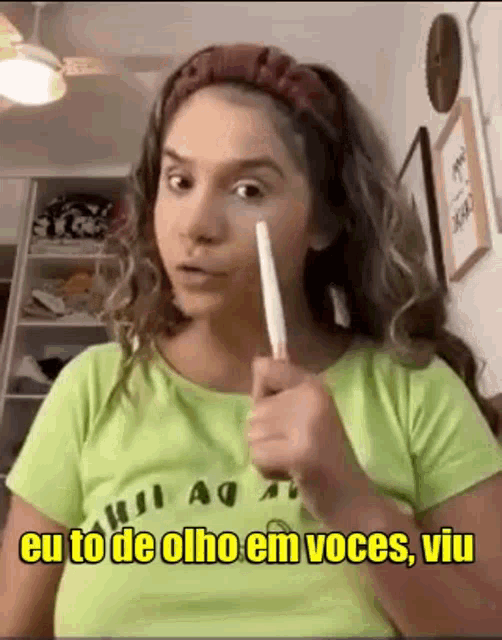 a woman in a green shirt is holding a stick in her hand and says eu to de olho em voces viu .