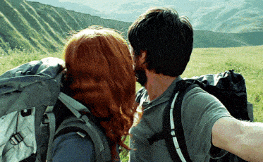 a man and woman with backpacks are looking at a mountain