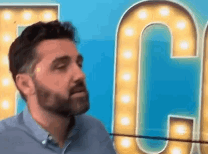 a man with a beard is standing in front of a large lighted letter c