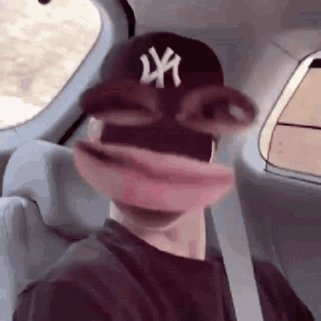 a man wearing a ny hat and glasses is sitting in a car with his mouth open .