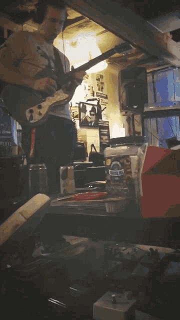 a man is playing a guitar in a room with a bottle of blue bell on the table