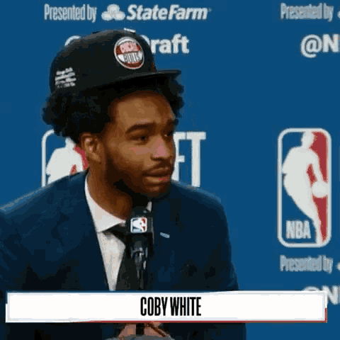 a man in a suit and tie is talking into a microphone with the name coby white on the bottom of the screen