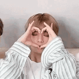 a man in a striped shirt is making a heart shape with his hands .