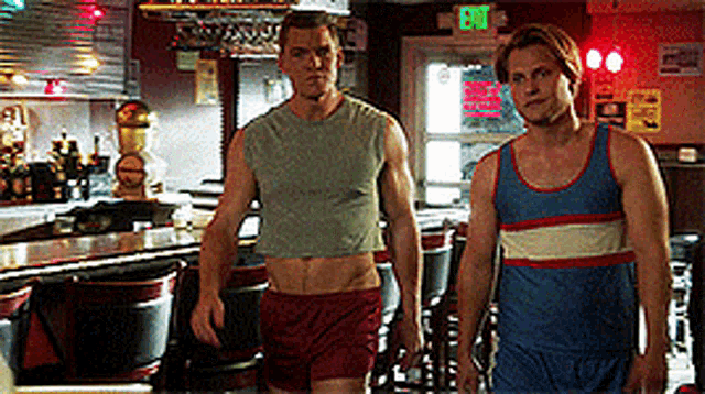 two men are standing in front of a bar with an exit sign above them