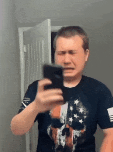 a man in an american flag shirt is taking a picture of himself with his phone .