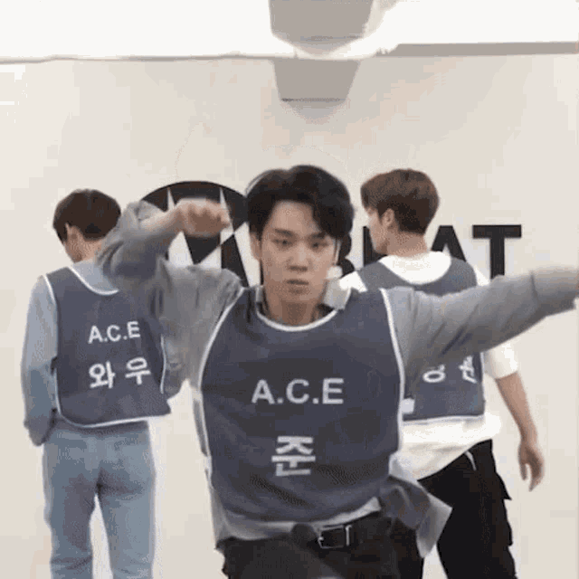 a man wearing a blue vest with the word a.c.e on it is dancing in a room with other men .