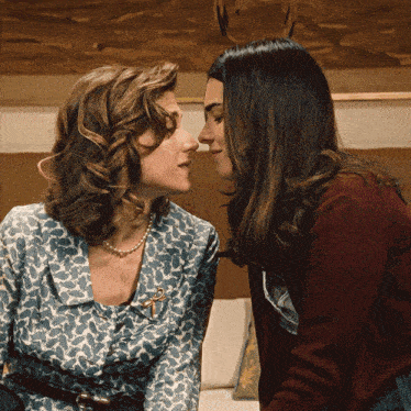 two women are looking at each other and one has a brooch on her collar