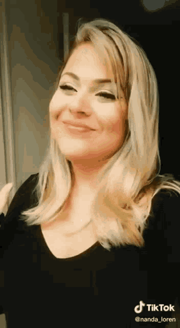 a woman with long blonde hair is smiling and wearing a black shirt .