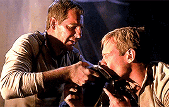 two men are standing next to each other and one of them is pointing at the other 's face .
