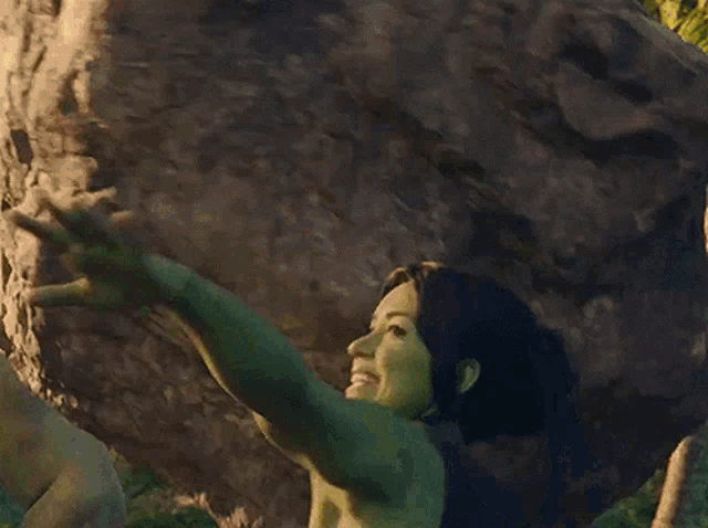 a woman with green hair is standing in the jungle holding a large rock in her hand .