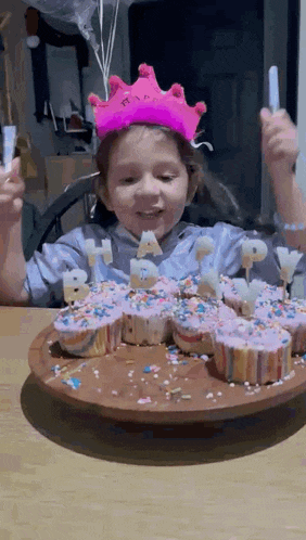 a little girl wearing a pink crown is blowing out candles on her birthday cake
