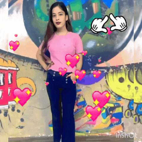 a girl in a pink shirt and blue jeans is standing in front of a wall with graffiti on it