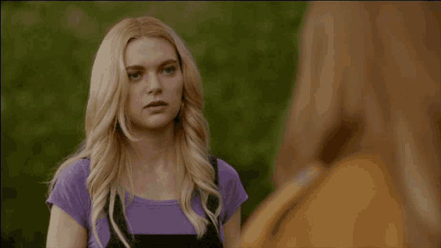a blonde woman in a purple shirt stands next to another blonde woman
