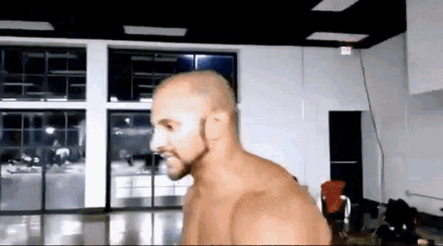 a bald man with a beard is standing in a room with a lot of windows .