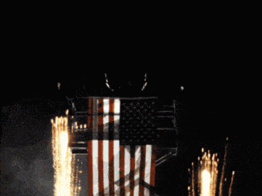 an american flag is surrounded by fireworks in the dark