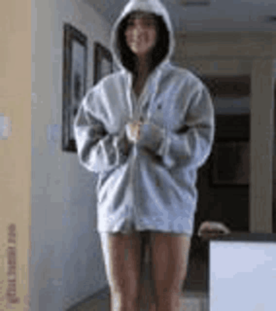 a woman is standing in a room wearing a hoodie and shorts .