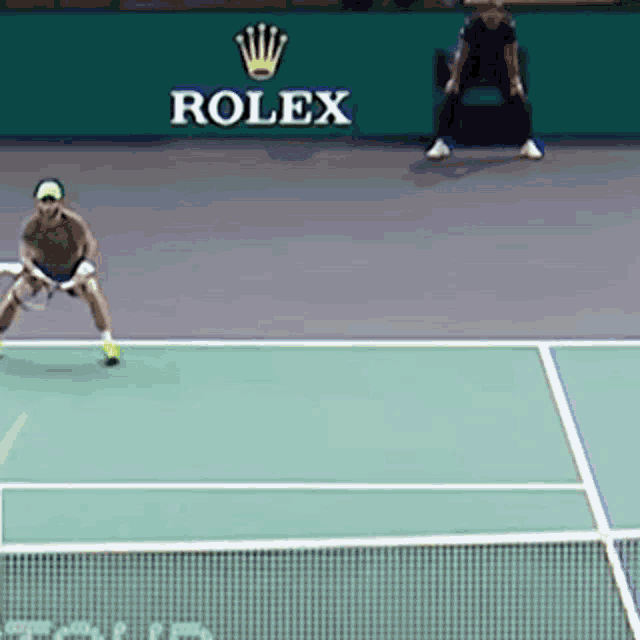 a man is playing tennis on a court with a rolex sign in the background