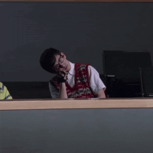 a man wearing glasses and a vest is sitting in front of a monitor