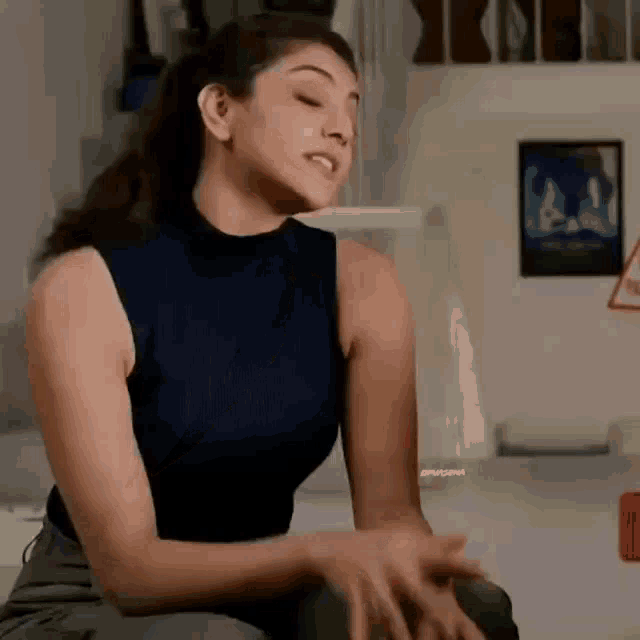 a woman in a blue sleeveless top is sitting on a couch .