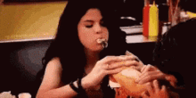 a woman is sitting at a table eating a sandwich with a bottle of ketchup in the background .